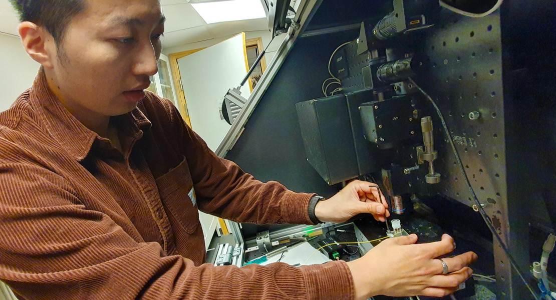 Il ricercatore Lee-Lun Lai regola il puntatore laser sulla macchina da stampa 3D Lee-Lun Lai dimostra la configurazione per stampare microstrutture di vetro di silice su una fibra ottica.